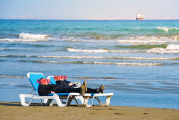 Adult men and women are lying on the sun loungers on the beach near the sea with the inscription GDPR instead of the face