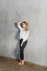 Model blonde blue jeans white shirt standing gray wall by window  copy space.