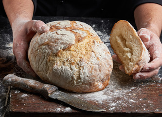 cook in a black tunic holds fresh baked bread