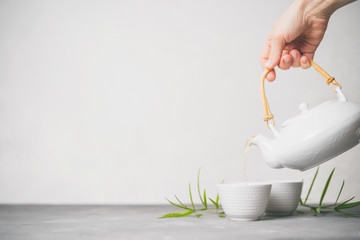 Female hand pouring green tea from a teapot into cups on white background with copy space. Asian tea set.