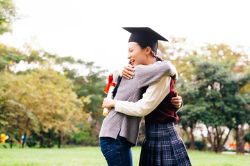 Smiling and happy Asian female graduate student hugging and embracing people with graduation hat in nature park.