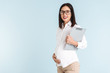 © Drobot Dean - Pregnant business woman isolated over blue wall background holding clipboard.