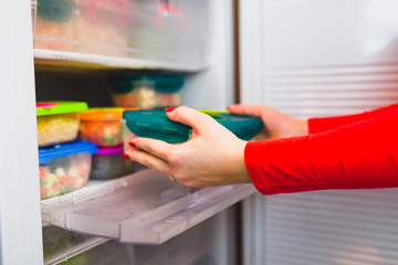 Woman placing container with frozen mixed vegetables in refrigerator.