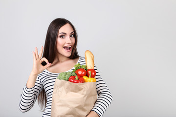 Wall Mural - Beautiful woman holding grocery shopping bag on grey background