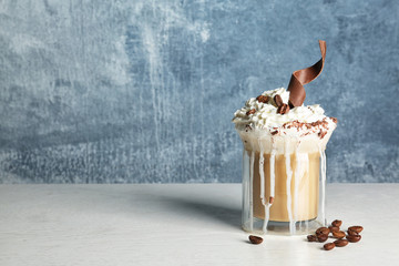 Glass cup of tasty coffee with whipped cream and chocolate on table against color background. Space for text