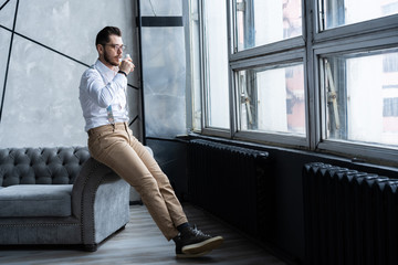 Wall Mural - Feeling lonely. Stylishly dressed young man holding a glass while sitting on sofa.