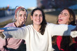 © 2Design - Outdoor portrait of three friends fun girls taking photos with a smartphone at bright sunset.