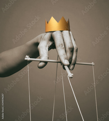 Concept of manipulation. Hand with crown holds strings for manipulation. Black and white.