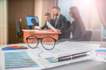 Business concept. Business people discussing, financial chart near 

dollars, focus on glasses on foreground