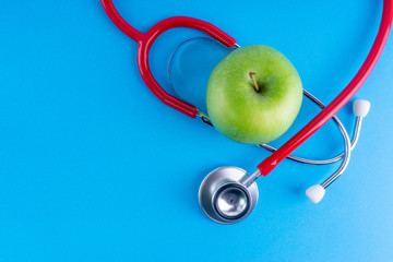 Green Apple with medical stethoscope isolated on blue background for healthy eating. Selective focus and crop fragment. Healthy, Diet and copy space concept