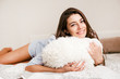 © zadorozhna - Young smiling woman lying with pillow in bed in her bedroom. Happy morning.