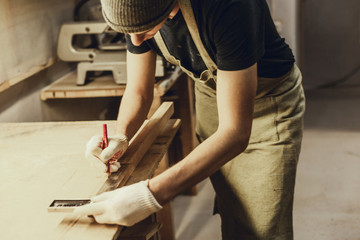 Wall Mural - Crop young man in apron making marks on plank with pencil and ruler while working in professional joinery