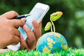 Student Hand holding smartphone for studying or researching seeding plant on Globe model in outdoor lab on sunny  green grass, Green save world environment ecology day, Life on earth concept