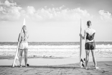 Wall Mural - Friends surfers standing on the beach with surfboards preparing to surf on high waves - Healthy couple surfing together - Black and white editing - Concept of sporty people lifestyle