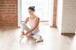 © Rithor - Horizontal shot of young gently ballerina wearing pink top and pointe sits on wooden floor of dance sport studio. Female dance teacher teaches at school dance. People and their profession, vocation