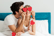 © Tijana - Young happy couple sitting on the bed, holding red hearts