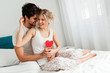 © Tijana - Young happy couple sitting on the bed, holding red hearts