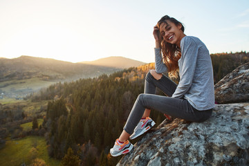 Wall Mural - woman sits on edge of cliff against background of sunrise