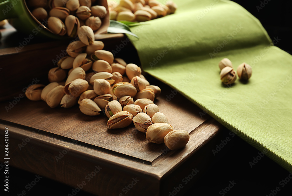 Overturned cup with tasty pistachio nuts on wooden board