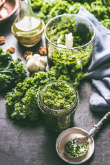 Sticker - Raw kale eating recipes. Green kale pesto in glass on dark rustic kitchen table background with ingredients, top view. Kale preparation. Healthy detox vegetables . Clean eating and dieting concept.