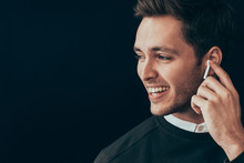 Closeup Horizontal Portrait Of Young Handsome Man Smiling And Have A Call With A Colleague Isolated On Black Background Holding Wireless Earphone With Finger. Businessman Using Wireless Headphone.