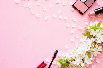 Black eyelashes mascara, eye shadows and lipstick with fresh cherry blossoms, petals on pink pastel desk. Mockup for special offers as advertising or other ideas. Empty place for text, logo or quote. 