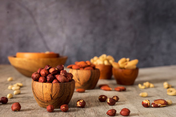 Wall Mural - Hazelnuts, cashews, Brazil nuts and almond wooden bowls on a gray background.