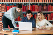 © Aleksandr - University students sitting together at table with books and laptop. Happy young people doing group study in library