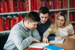© Aleksandr - University students sitting together at table with books and laptop. Happy young people doing group study in library