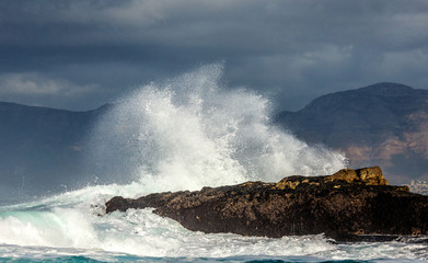  Big waves break on the rocks in the sea against the backdrop of the coastline. Beautiful seascape.  A beautiful moment. Very dynamic photo. Cape Town. False Bay. South Africa.