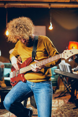 Sticker - Close up of bass guitarist playing guitar while sitting on the chair. Home studio interior.