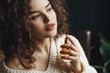 © Victoria Fox - Close up portrait of young beautiful sensual curly woman using, holding luxury perfume in orange glass bottle. Model wearing warm winter knitted sweater. Copy, empty space for text