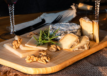 Some Kinds Of The Blue Cheeses With Halves Of The Walnuts And Rosemary, Two Glasses With Red Wines, Knife And Fork On The Wooden Desk