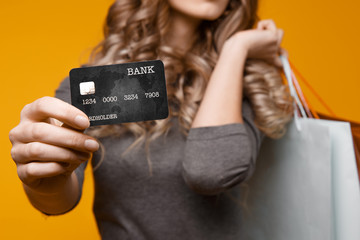 Wall Mural - lose-up portrait of happy young brunette woman holding credit card and black shopping bags, looking at camera, isolated on yellow background