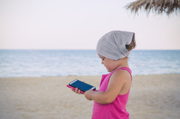 little girl in a red dress holding a phone in her hands on the sea beach