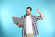 © New Africa - Emotional young man with laptop celebrating victory on color background