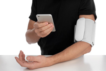 Man checking blood pressure with modern monitor and smartphone at table against white background, closeup. Cardiology concept