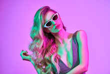 High Fashion. Woman In Colorful Bright Neon Purple Light. Glamour Sexy Disco Girl In Trendy Dress, Stylish Sunglasses, Makeup. Creative Fashionable Portrait