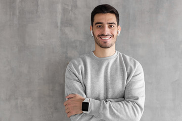 Wall Mural - Portrait of smiling handsome man wearing smart watches, standing with crossed arms against gray textured wall