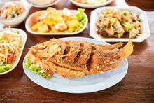 Fired Fish With Other Delicious Thai Foods On Wooden Table.