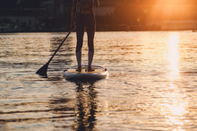 SUP Silhouette Of Young Girl Paddle Boarding At Sunset