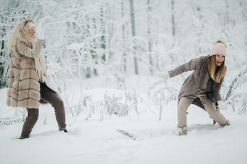 Image of two blondes throwing snow on walk in winter forest