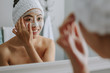 © Jacob Lund - Reflection of a woman in bathroom mirror applying face pack