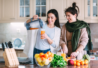 Two beautiful young woman preparing detox juice and having fun at kitchen