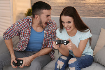 Wall Mural - Emotional couple sitting on sofa and playing video game at home