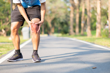 Young fitness man holding his sports leg injury. muscle painful during training. Asian runner having knee ache and problem after running and exercise outside morning. sport and healthy concepts