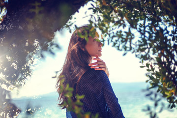 Beautiful brunette girl, portrait through the trees on a background of nature.  Spring, beauty, fashion concept