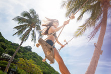 Young Beautiful Happy Woman In Top And Shorts Swinging On A Swing On The Shore Of A Tropical Sea During Vacation. Travel And Vacation Concept
