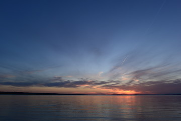 Wall Mural - Glowing sunlight  in the clear blue twilight sky in the silence of the summer evening before nightfall on a lake