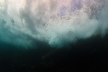 Underwater View Of Waves Crashing Against Rocks Producing Bubbles, Foam And Spray